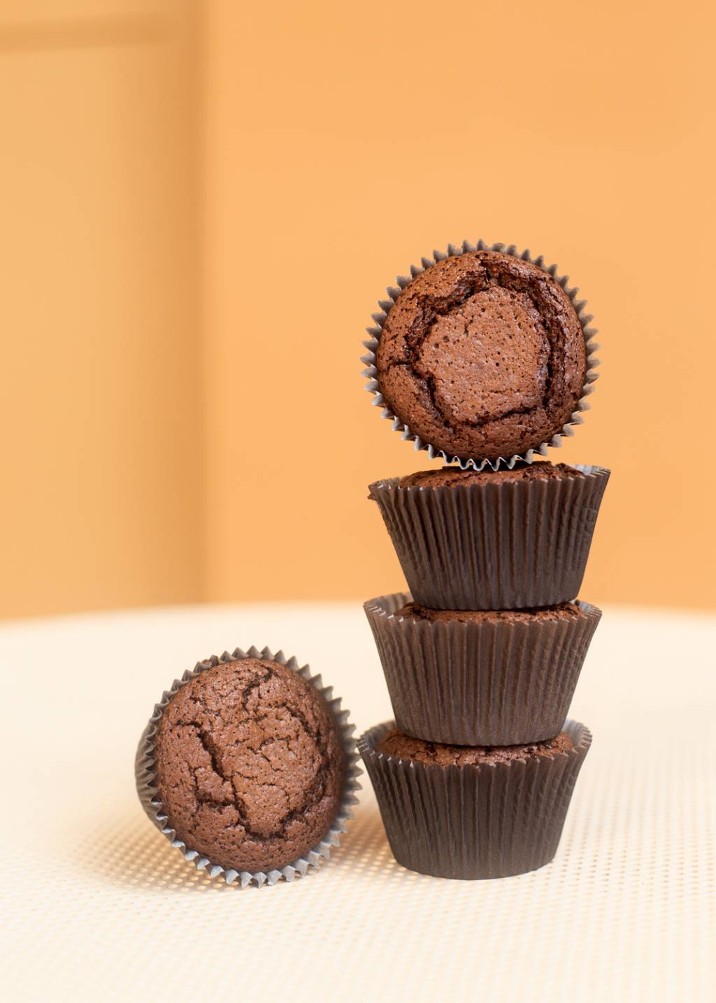 Martoca – Padaria Artesanal Quatro brownies de chocolate em forminhas empilhados ao lado de outro brownie.