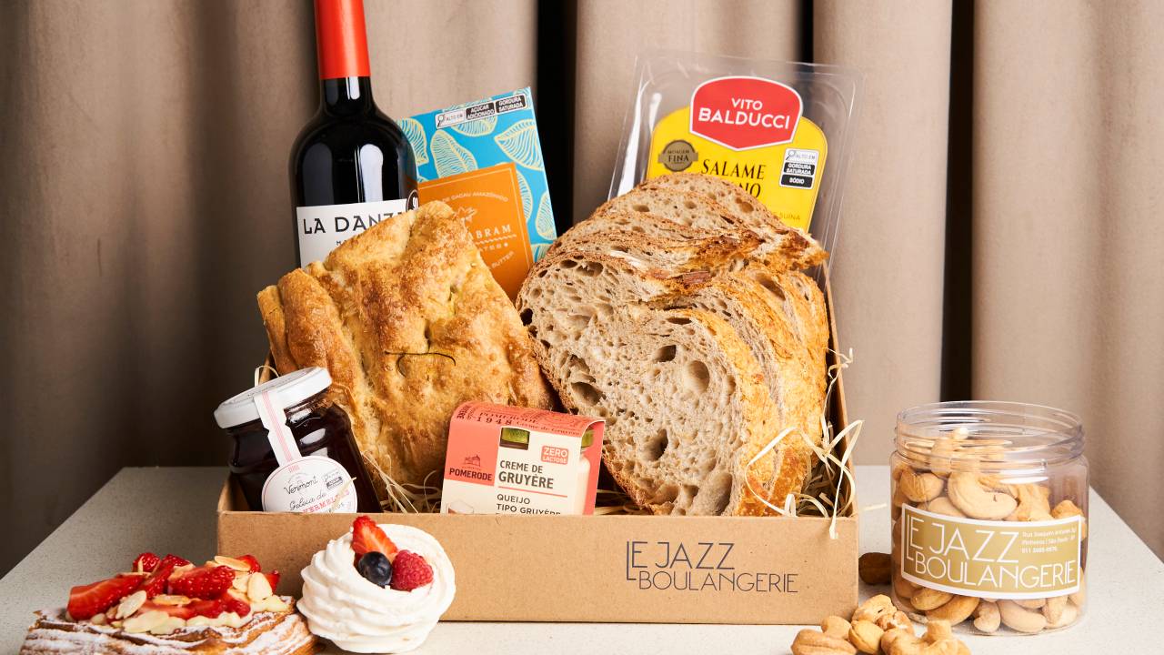 Cesta com produtos como vinhos, pães e doces em cima de uma mesa