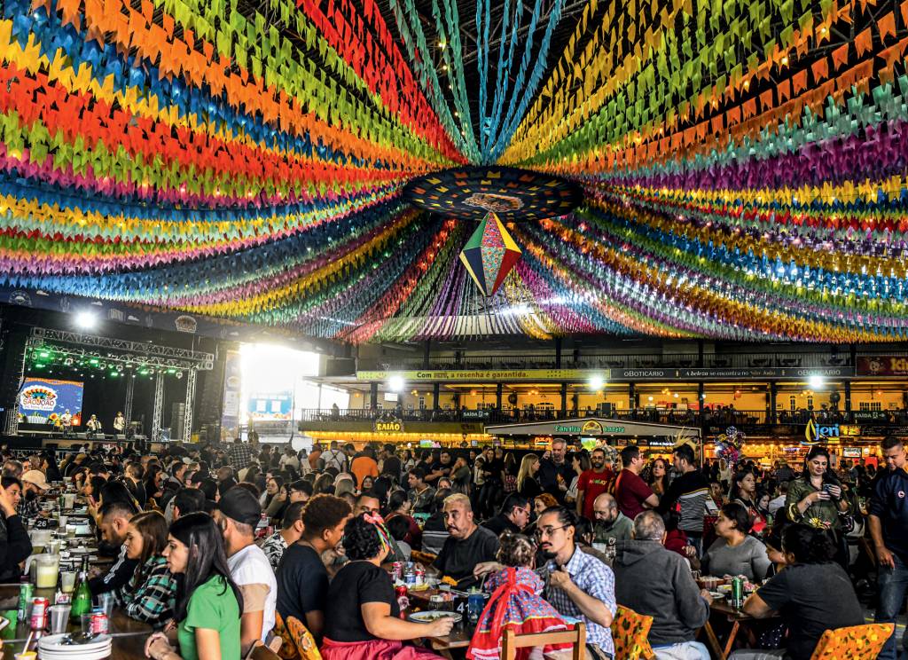 Festa Junina – Centro de Tradições Nordestinas Festa Junina do Centro de Tradições Nordestinas com bandeirinhas coloridas no teto e pessoas sentadas em mesas no salão