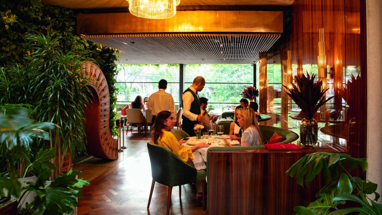 Salão do restaurante Giugiu, com chão de taco e pessoas sentadas em mesa à direita.