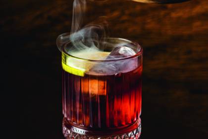 Caetano's Bar Copo de drinque avermelhado com fumaça saindo.