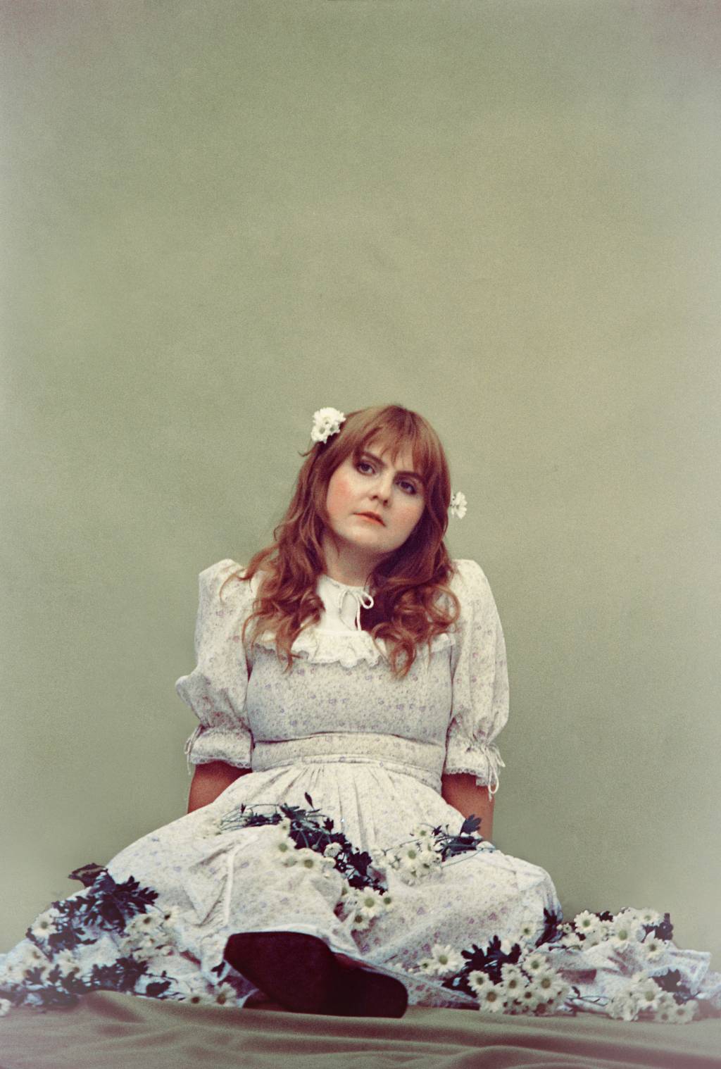 Julia Benford-Crédito Elisa Maciel-Divulgação (23) Mulher ruiva posa sentada com buquê de flores brancas na mão vestindo vestido branco