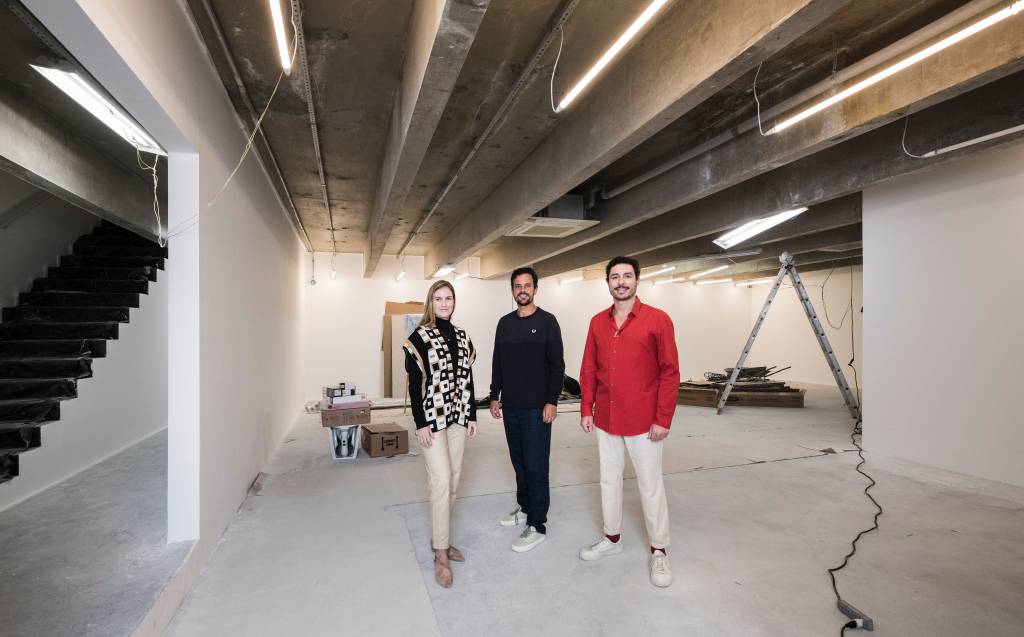 Sócios Galatea – Antonia Bergamin, Conrado Mesquita e Tomás Toledo (de camisa vermelha) Crédito Ding Musa-Divulgação (1) Três pessoas posam de pé em galpão em construção, a da direita vestindo camisa vermelha com calça branca e as demais com peças escuras