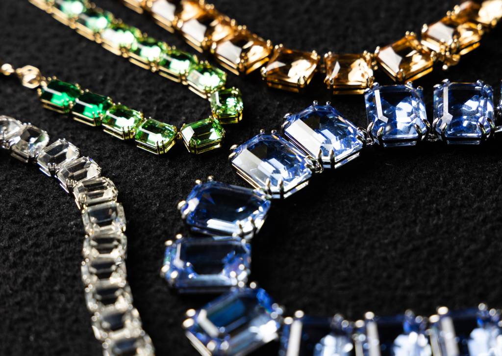 FLAVIASWAROVSKI24 Colares expostos em mesa preta nos tons dourado, verde e azul e pedras quadradas