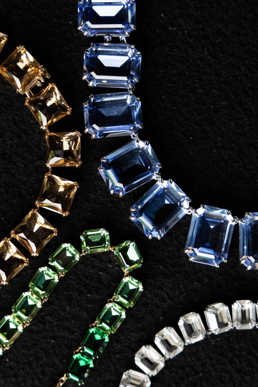 FLAVIASWAROVSKI25 Colares expostos em mesa preta nos tons dourado, verde e azul e pedras quadradas