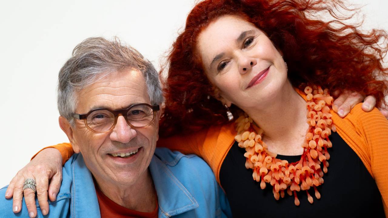 Homem grisalho de óculos e mulher ruiva de sorriem abraçados