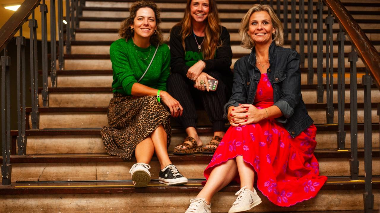 Três mulheres posam sentadas em uma escada