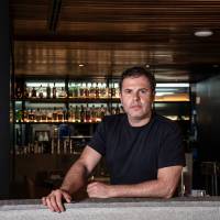 Comer & Beber 2024 - Cala del Tanit Homem em restaurante com bar atrás apoiado em balcão olhando para a foto.