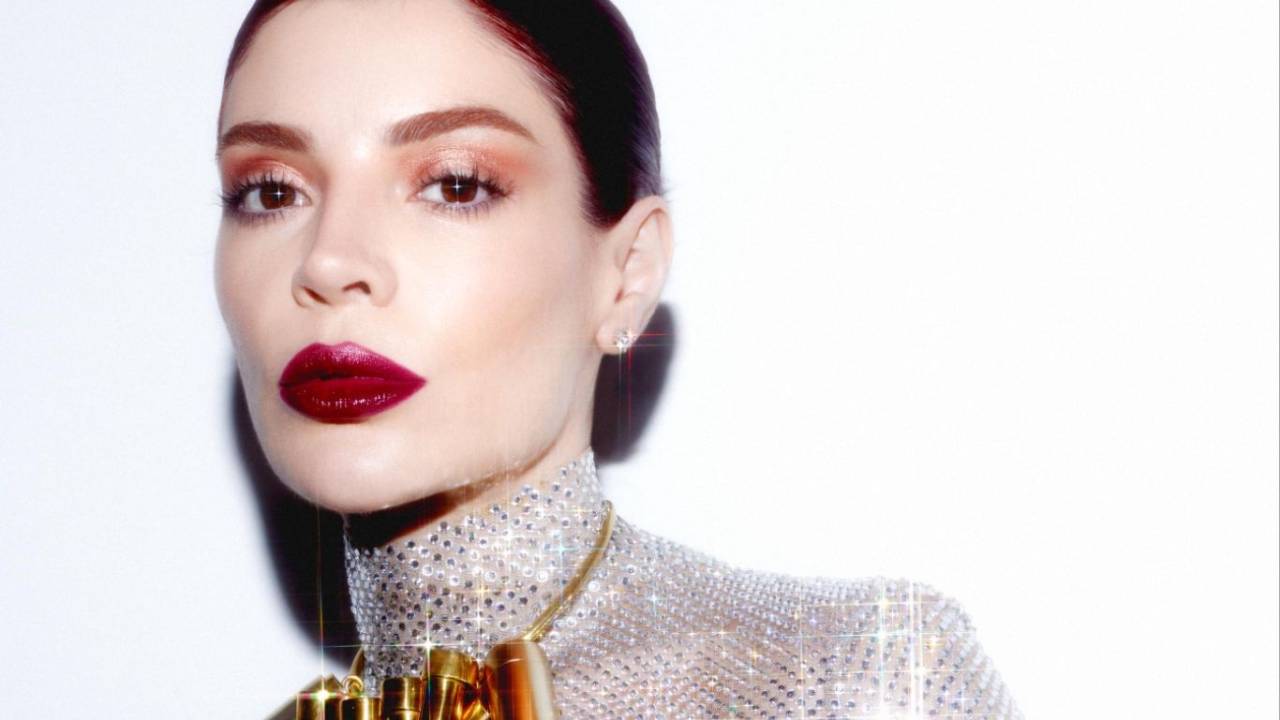 Moça de coque posa com blusa brilhante prateada e colar dourado