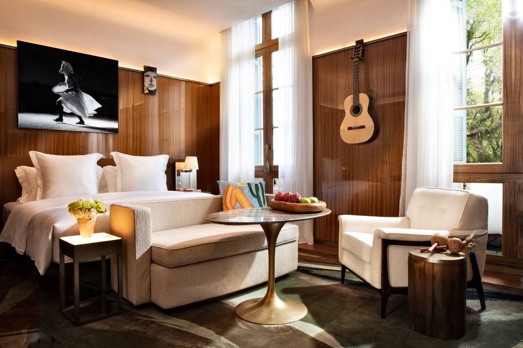 Grand premier room 2 Quarto Rosewood com sofá bege, mesa, janelas altas e violão na parede