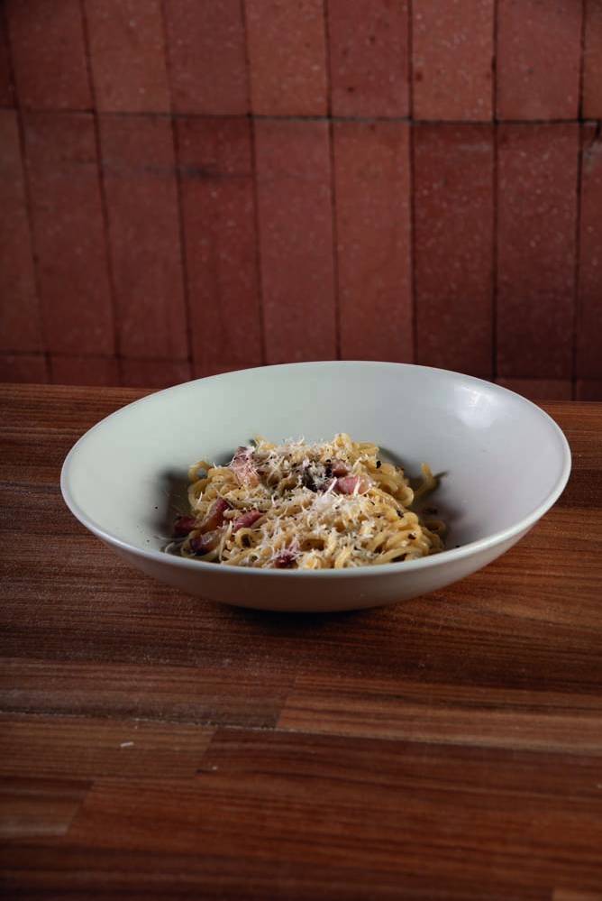 Comer & Beber 2024 – Shihoma Pasta Fresca Prato fundo de louça branca sobre mesa de madeira com espaguete à carbonara coberto por queijo ralado.