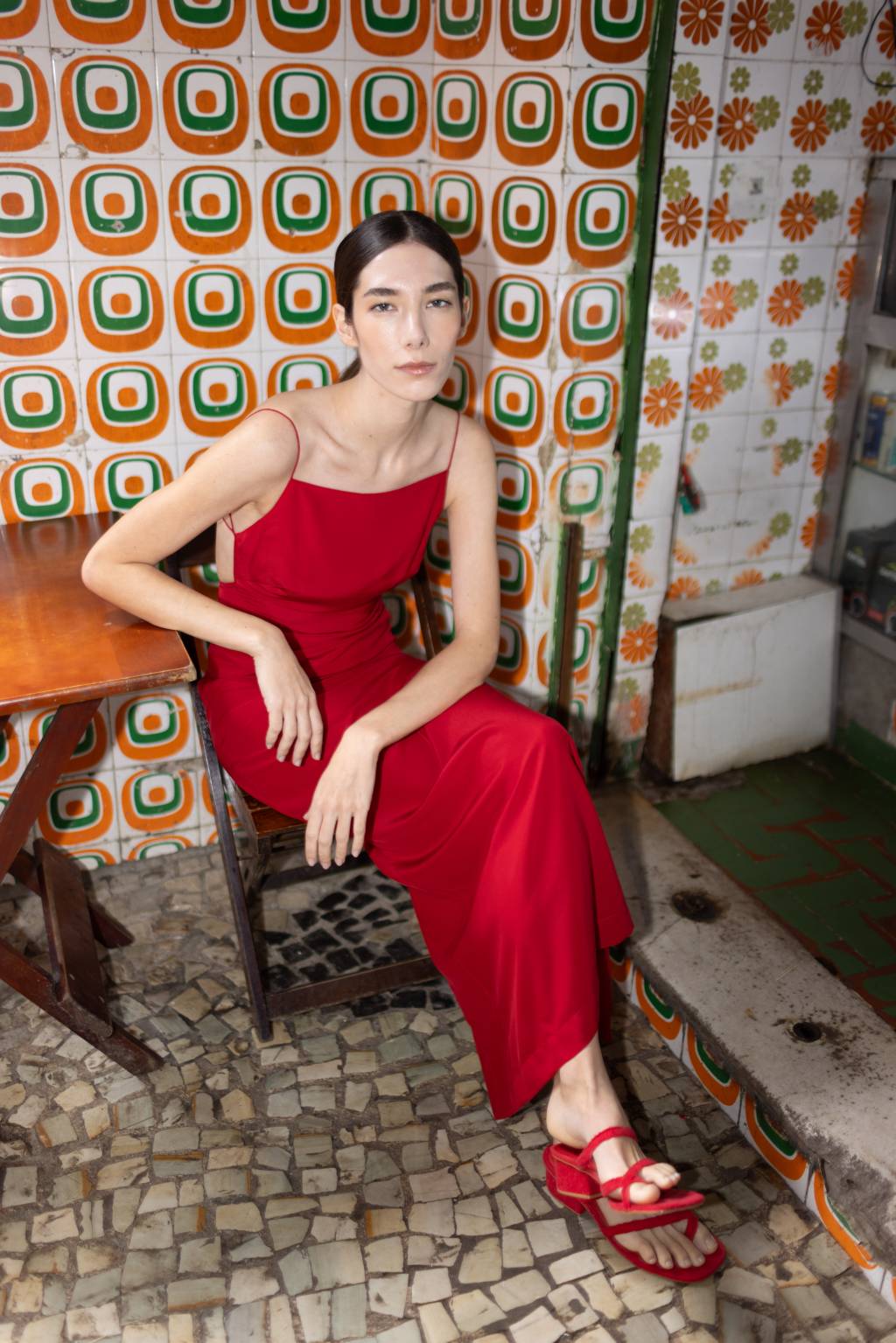 0P8A6351 Moça branca de vestido vermelho sentada de pernas cruzadas em mesa de madeira, de bar, com parede estampada