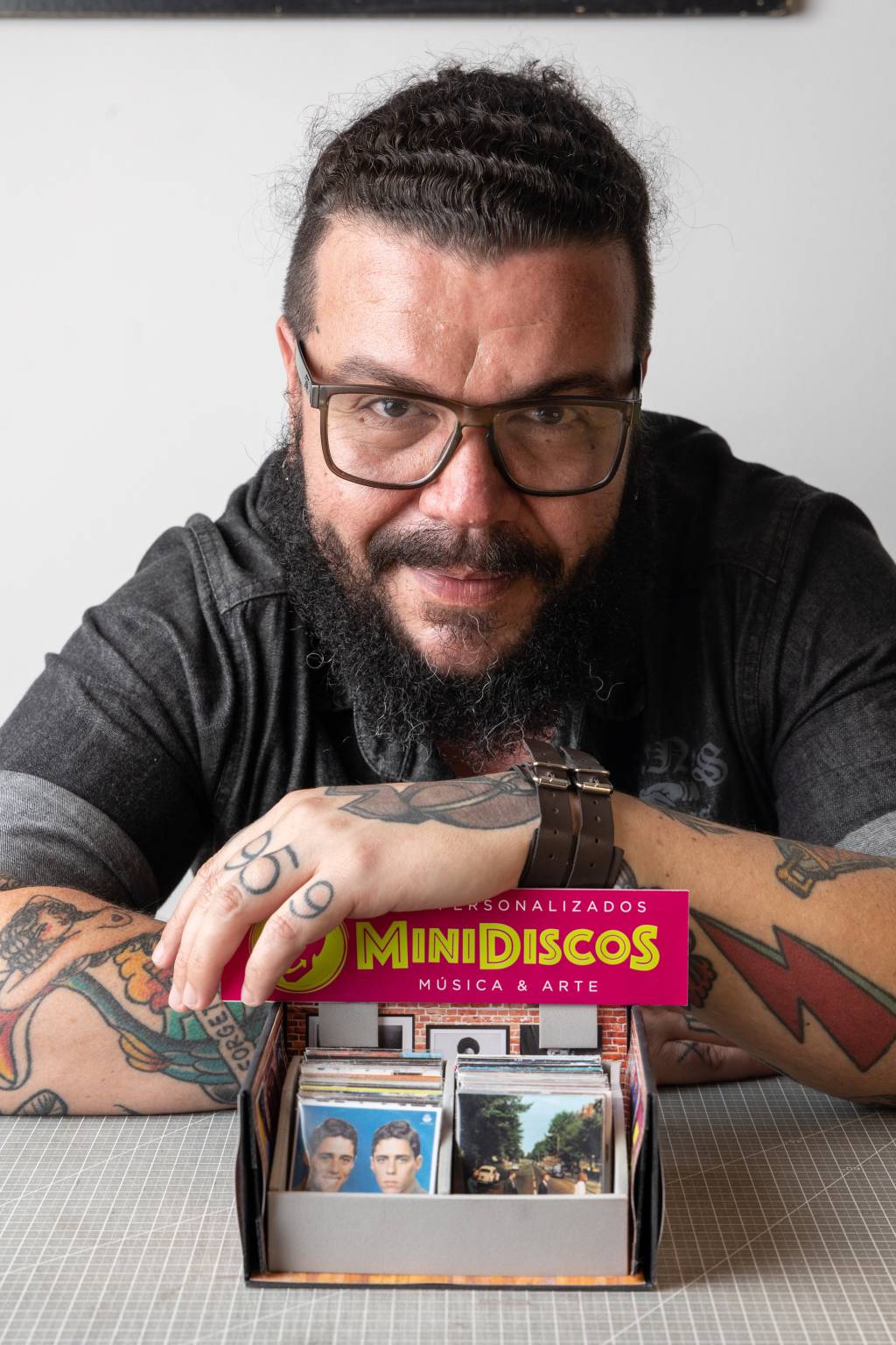 FELIPEFIUZAMINILP28 Homem de óculos e barba sorri segurando caixa repleta de minidiscos
