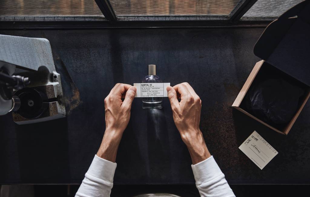 Le Labo_Labeling_300ppi_02 Par de mãos visto de cima manipulando rótulo de perfume