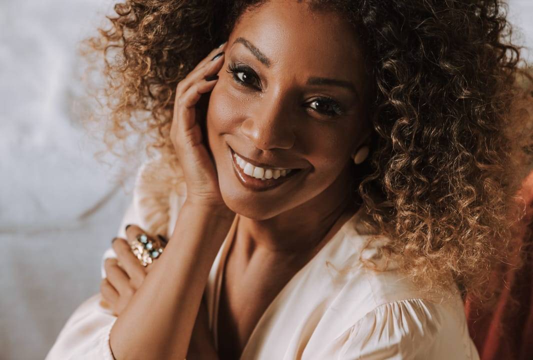 Mulher negra sorri vestindo peça bege claro