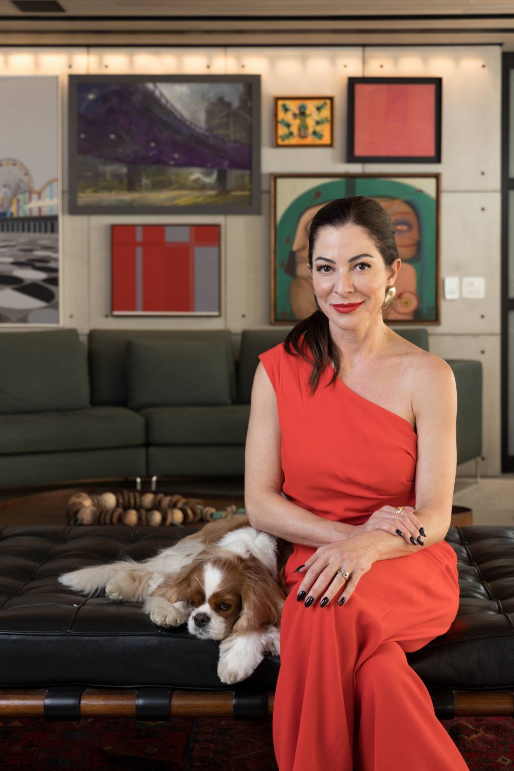 Ana Paula Padrão Crédito Wanezza Soares-VejaSP (04) Mulher branca de peça alaranjada posa com cachorro branco e marrom no colo em divã de couro preto e galeria de quadros e sofá verde ao fundo