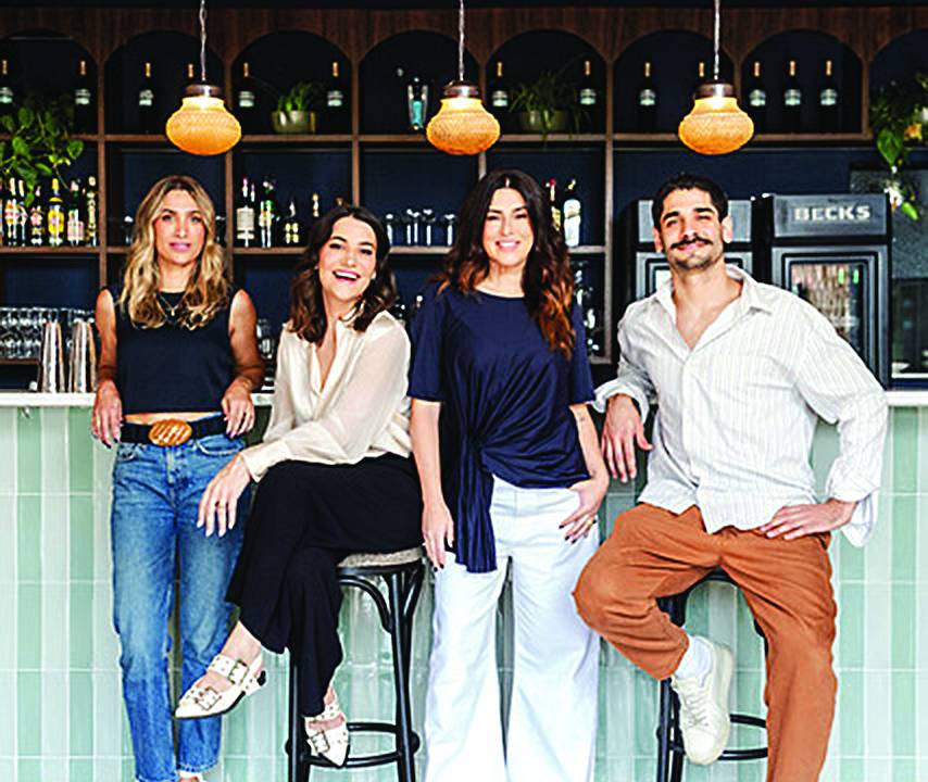 Quatro pessoas olhando pra foto e sorrindo com um bar atrás