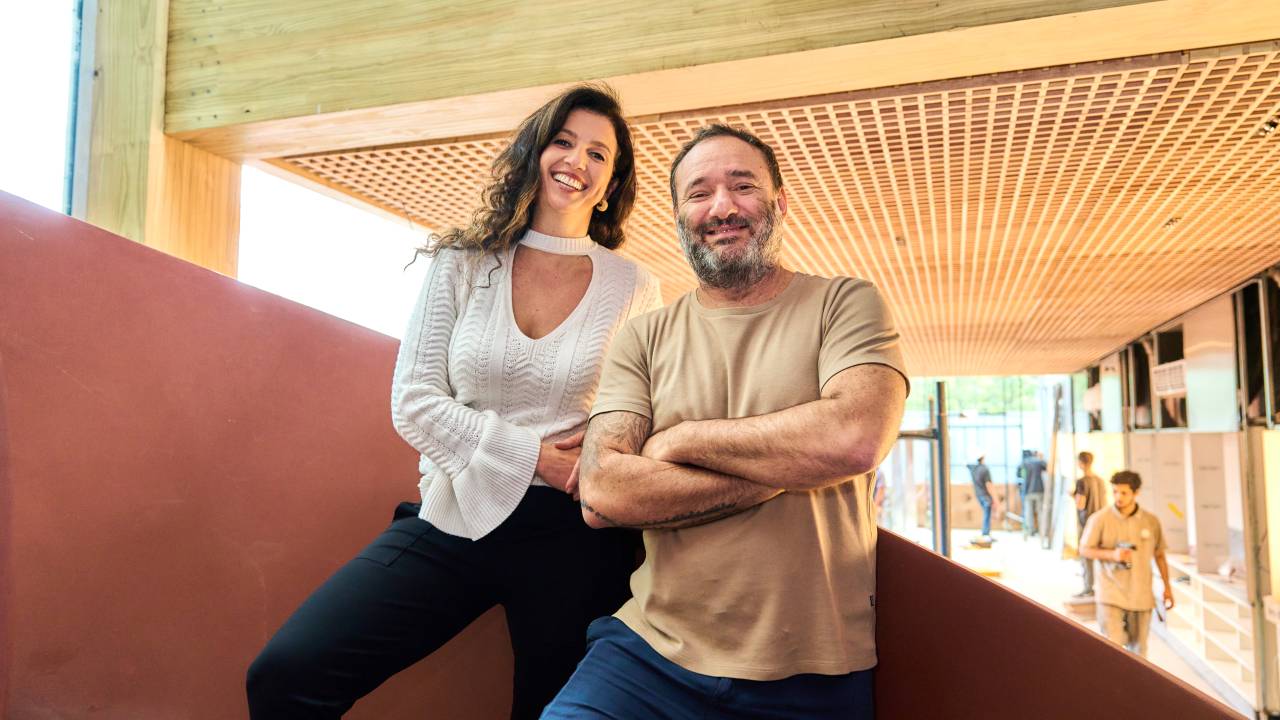 Mulher de branco e preto ao lado de homem com camiseta bege e jeans em uma escada
