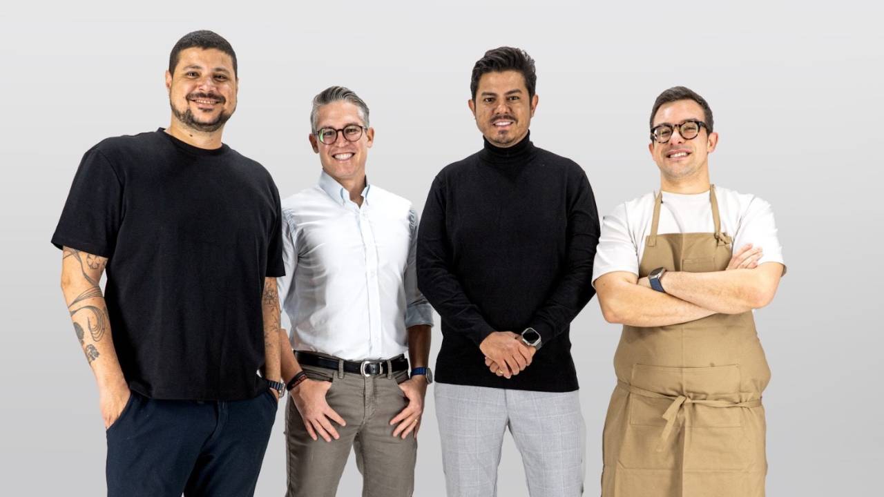 Quatro pessoas de pé e sorrindo olhando para a câmera