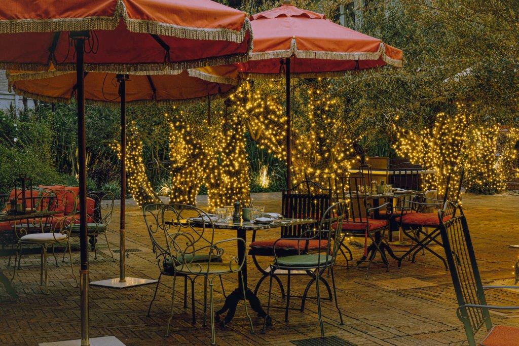 Toldos e mesinhas redondas em jardim com luzes de Natal