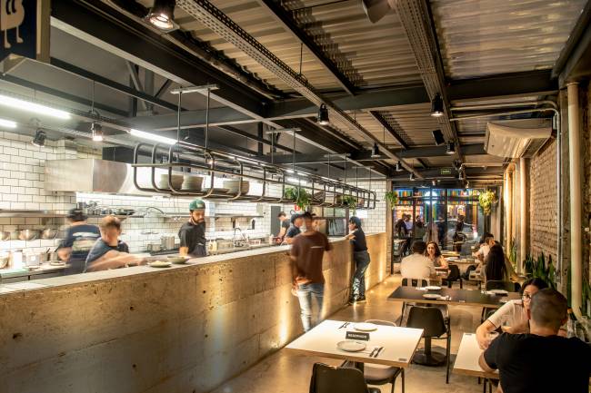 Espaço com mesas e cozinha aberta