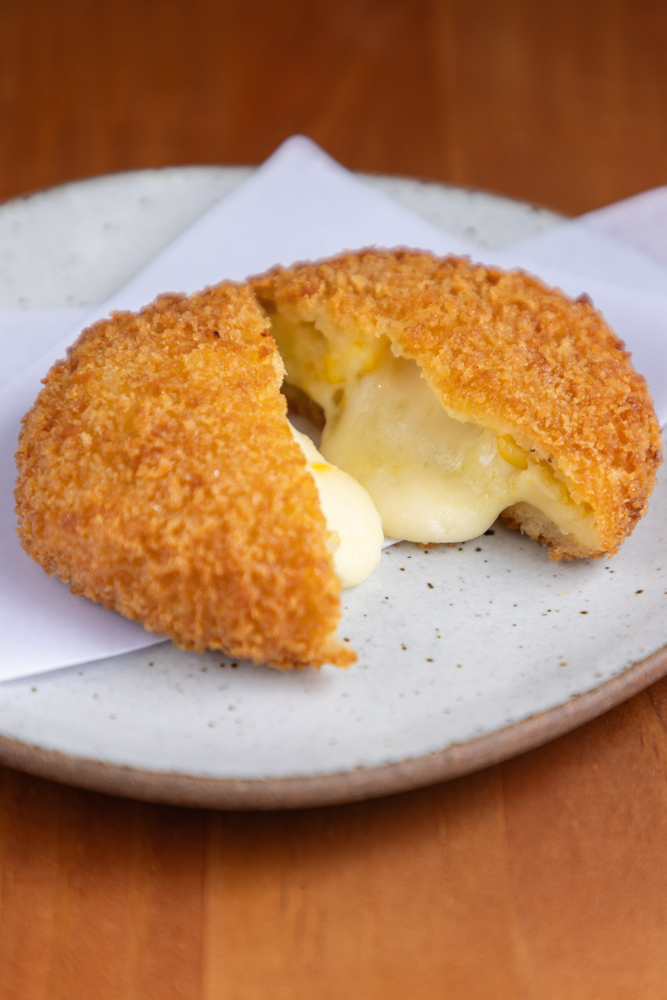 Korokke de milho e queijo _ Aizomê Café Salgado frito cortado ao meio em prato branco
