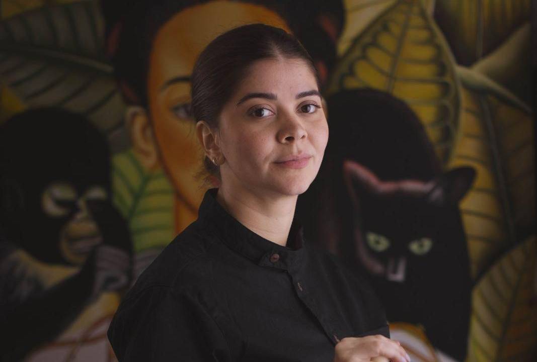 Mulher de cabelos pretos e presos sentada com uma garrafa nas mãos