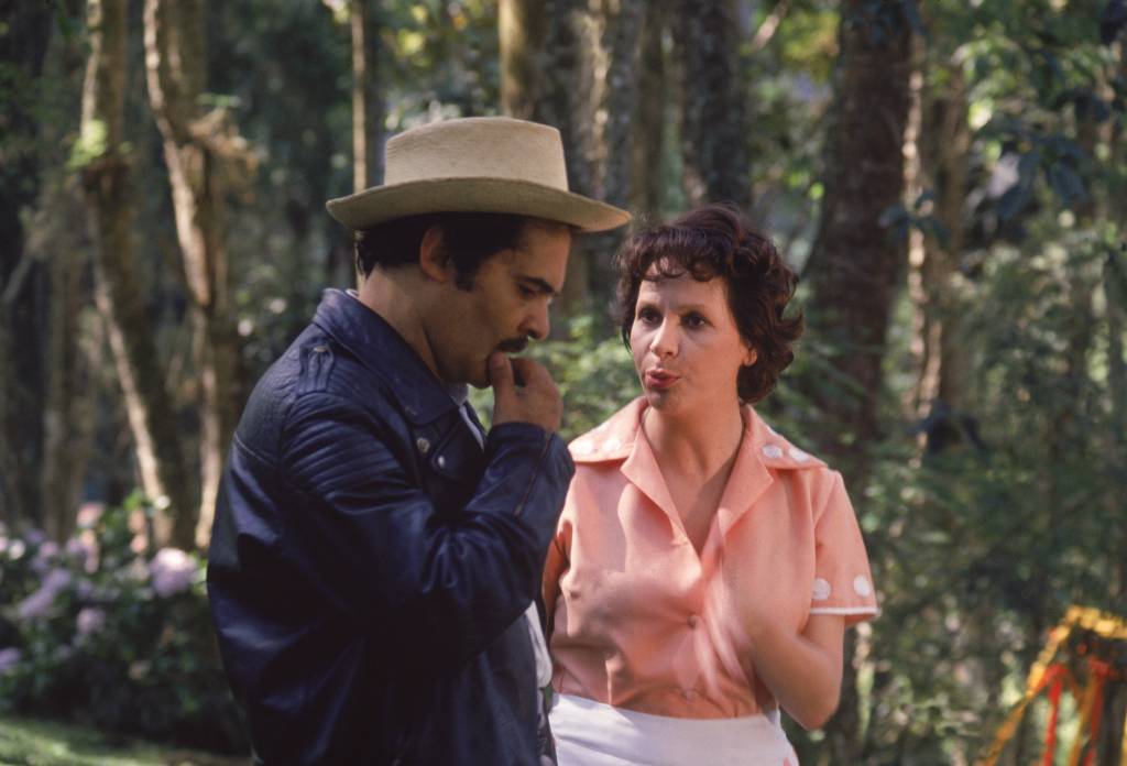 Othon Bastos e Arlete Montenegro na novela “Aritana”, da TV Tupi. Othon Bastos e Arlete Montenegro na novela Aritana, da TV Tupi, ele com chapéu e ela com peça rosa, ambos andando em floresta