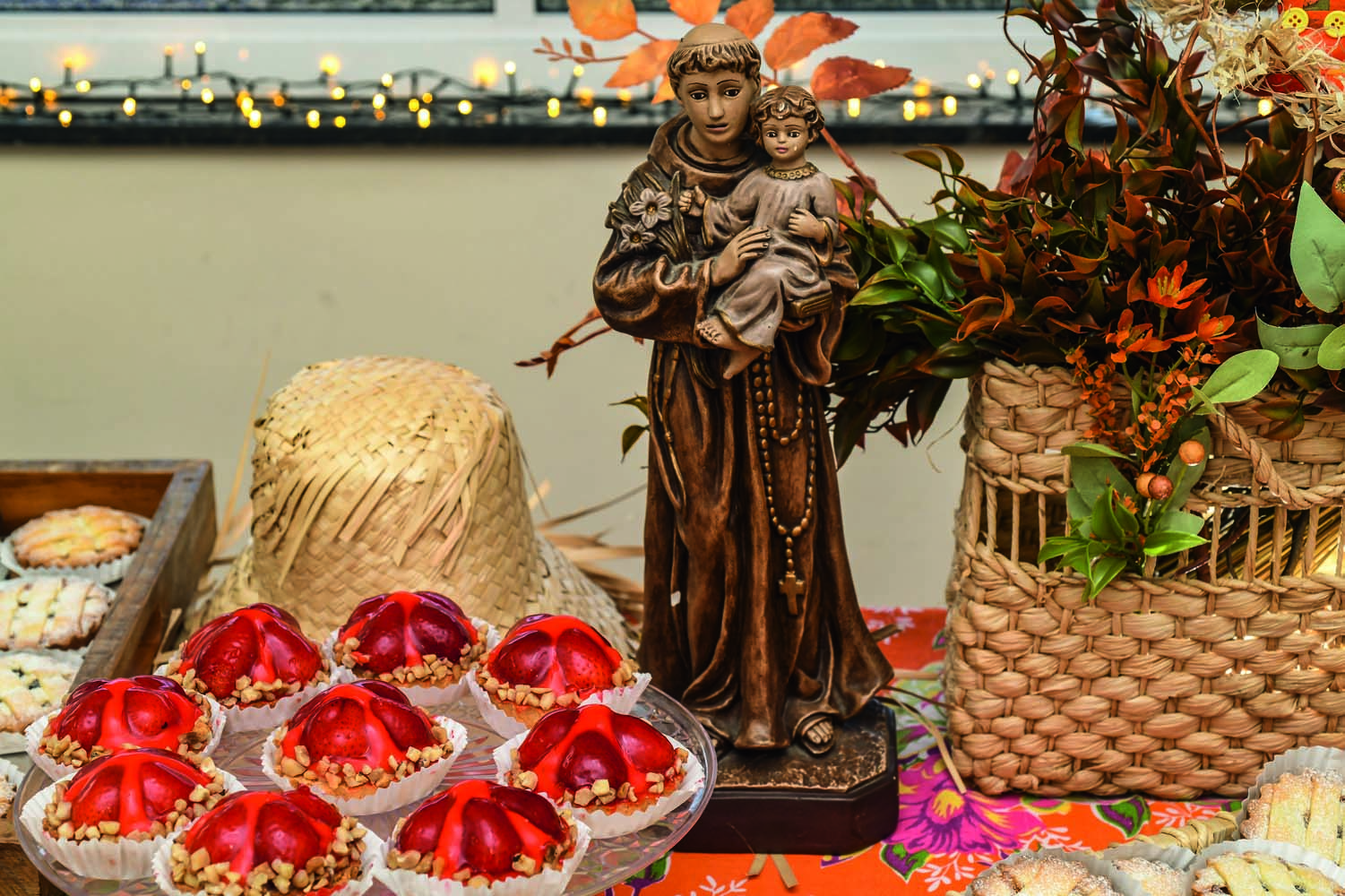 Santo e comidinhas ao lado e cesta de palha com flores
